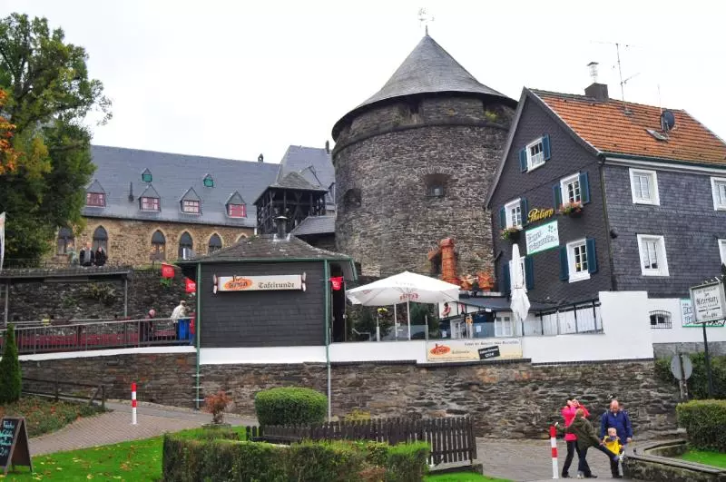 Steinernes Schloss Burg mit Rundturm neben Fachwerkhäusern und Außengastronomie