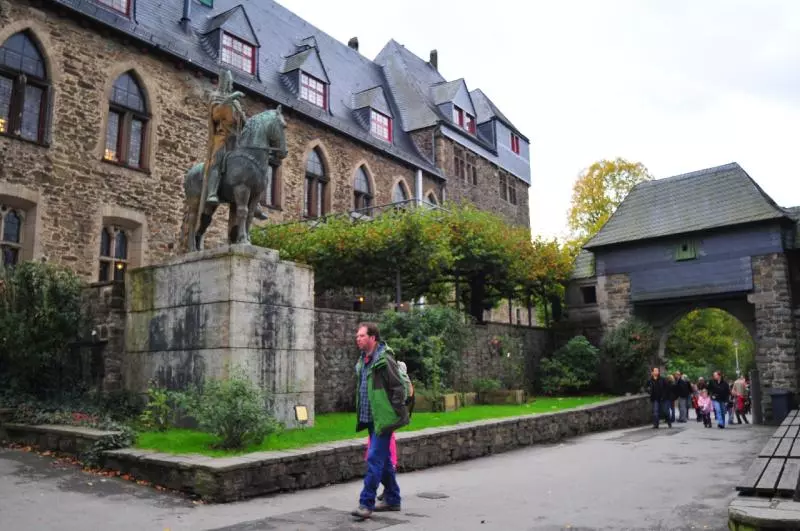 Besucher an einer Reiterstatue vor einem Torbogen von Schloss Burg