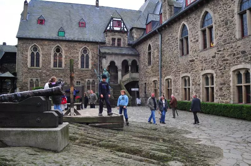 Besucher in einem Schlosshof mit gotischen Fenstern und ausgestellter Kanone